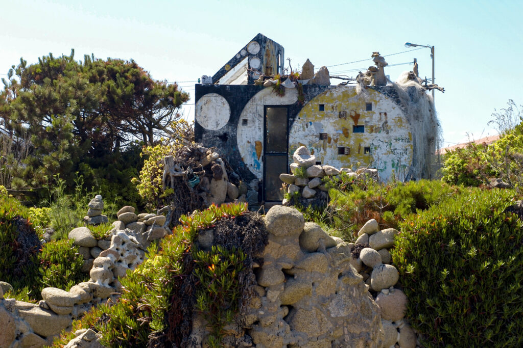 Ruins of Manfred Gnädinger’s house with stone sculptures and overgrown plants at Museo do Alemán in Camelle.