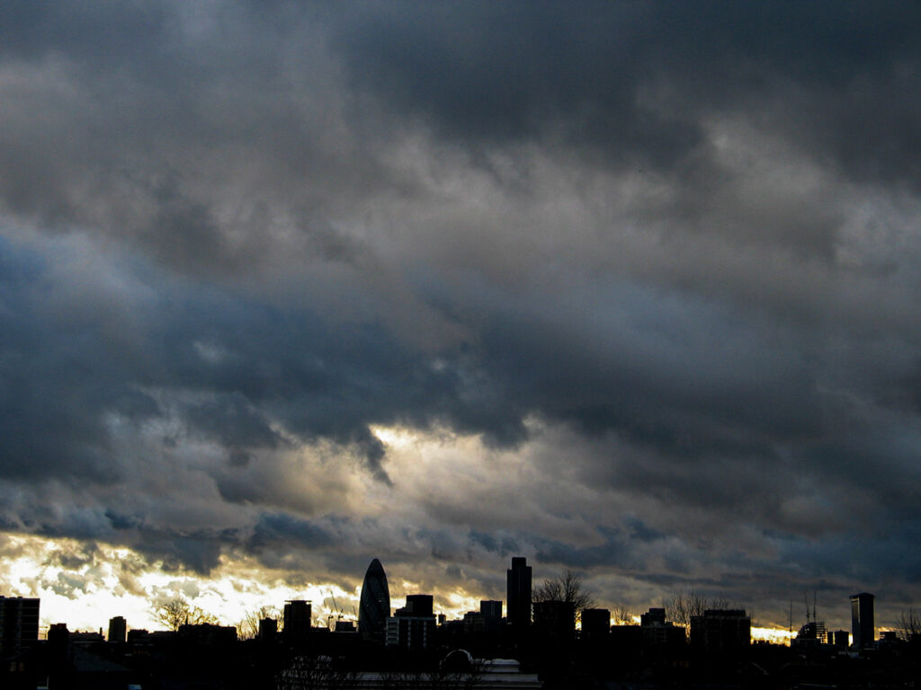 City of London skyline seen from Hackney on Saturday 20 December 2003 at 15:37, with The Gherkin, Tower 42, and One Canada Square silhouetted beneath thick stratocumulus and nimbostratus clouds. skyline seen from Hackney with the iconic buildings The Gherkin, Tower 42 and One Canada Square showcasing their iconic silhouettes.