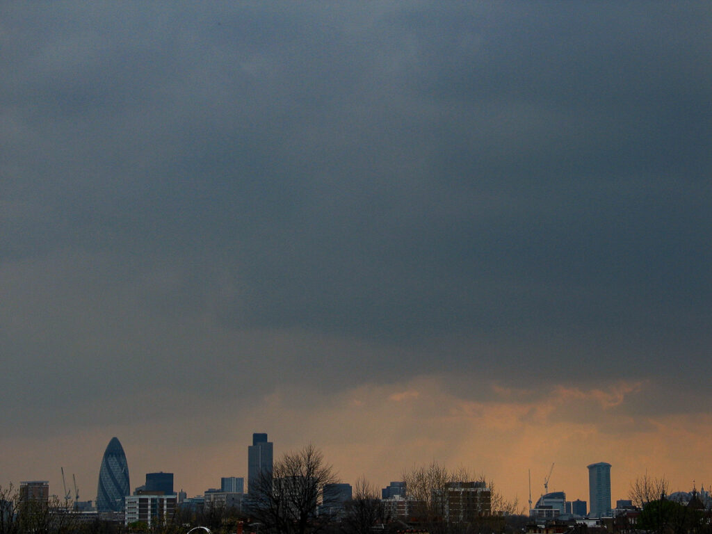 City of London skyline seen from Hackney on Tuesday 13 April 2004 at 16:04, featuring The Gherkin, Tower 42, and One Canada Square beneath scattered cumulus clouds on a clear afternoon.