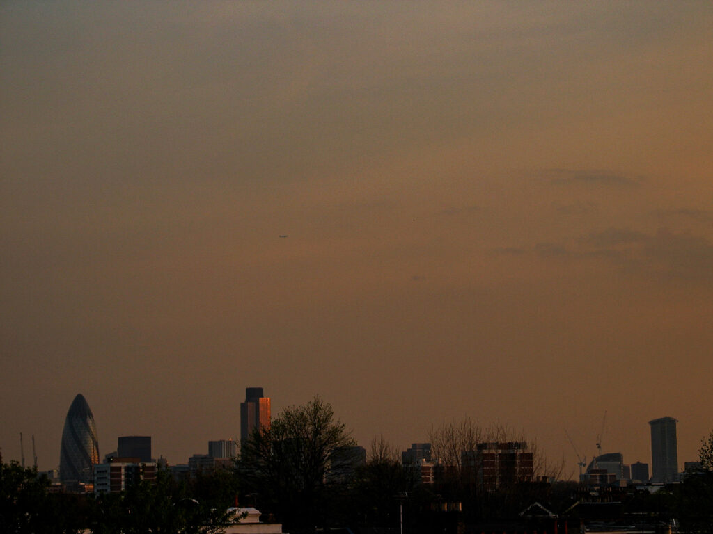 City of London skyline seen from Hackney on Friday 23 April 2004, with The Gherkin, Tower 42, and One Canada Square silhouetted against a golden dusk sky with scattered altocumulus clouds.