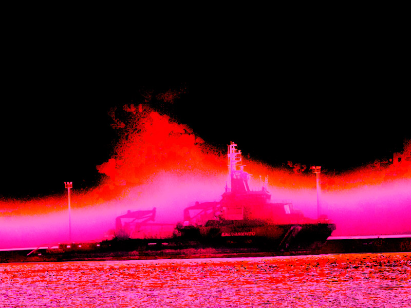 A ship at dock now radiates intense magenta and red hues, casting colored light across the waters and standing out against the surrounding darkness.