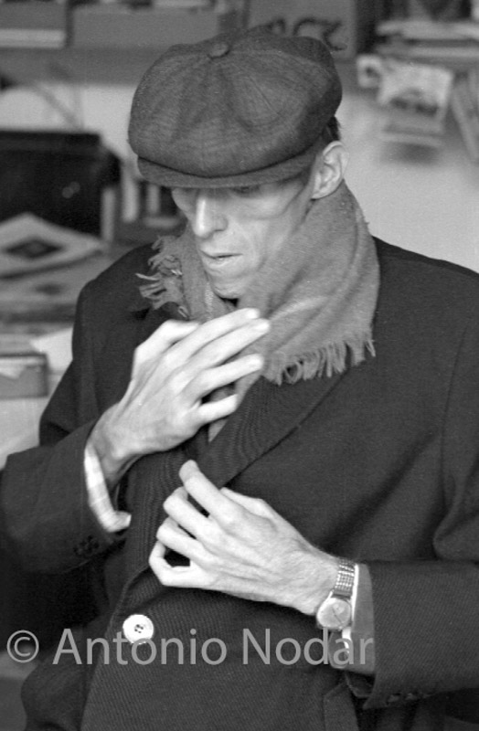 Carlos Moro adjusts his coat and scarf with both hands while sitting indoors in Barcelona.