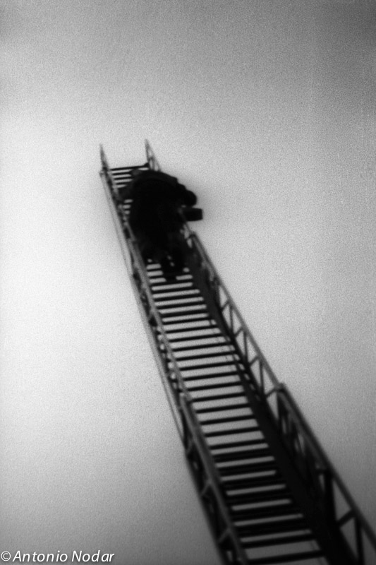 Blurred figure climbs a long metal staircase against a stark, empty sky in Paris, 1980s.