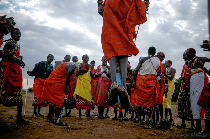 Samburu men in traditional clothing leap high into the air during the Adumu dance, surrounded by women in colorful shawls and beadwork in Kenya’s Rift Valley