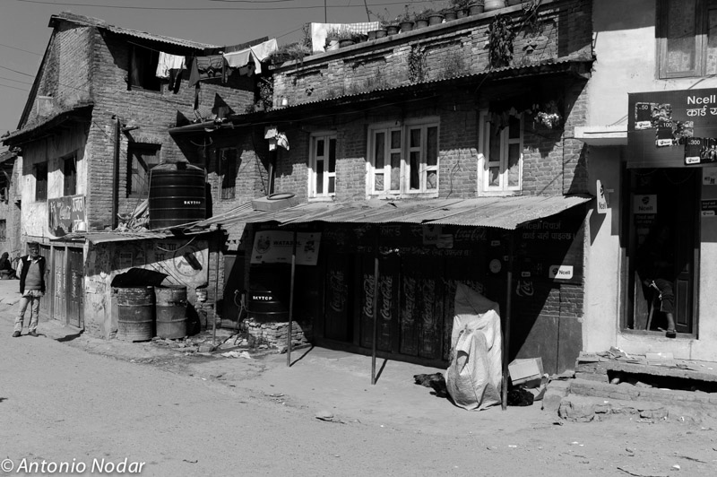 Traditional brick houses and local shops in Bungamati, Nepal, with a man walking on a sunlit street