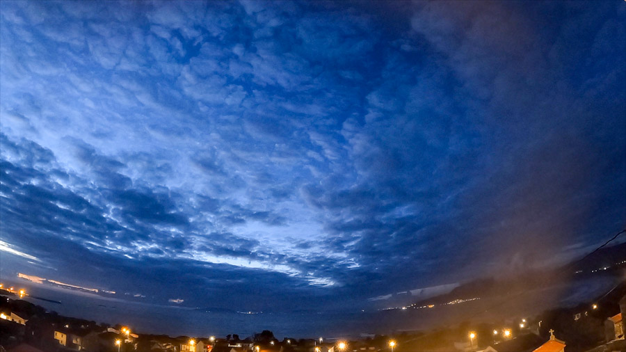 Blue‑hour panoramic view over Carnota Bay on the Costa da Morte with a textured layer of altocumulus stratiformis clouds filling the sky above the village lights of Sofán, Caldebarcos, Monte Pindo and distant Cape Fisterra.
