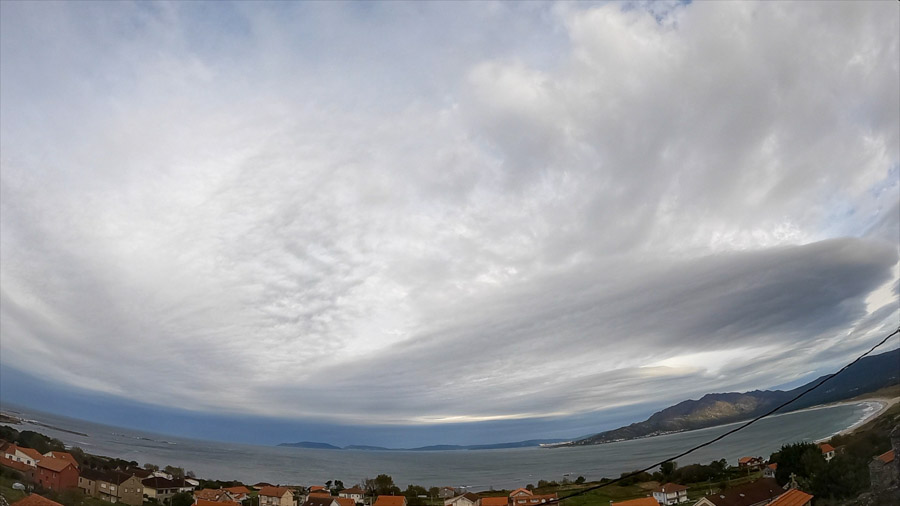 Midday panoramic view over Carnota Bay on the Costa da Morte with parallel bands of altostratus radiatus clouds above the rooftops of Sofán village, Monte Pindo, Caldebarcos and Cape Fisterra.