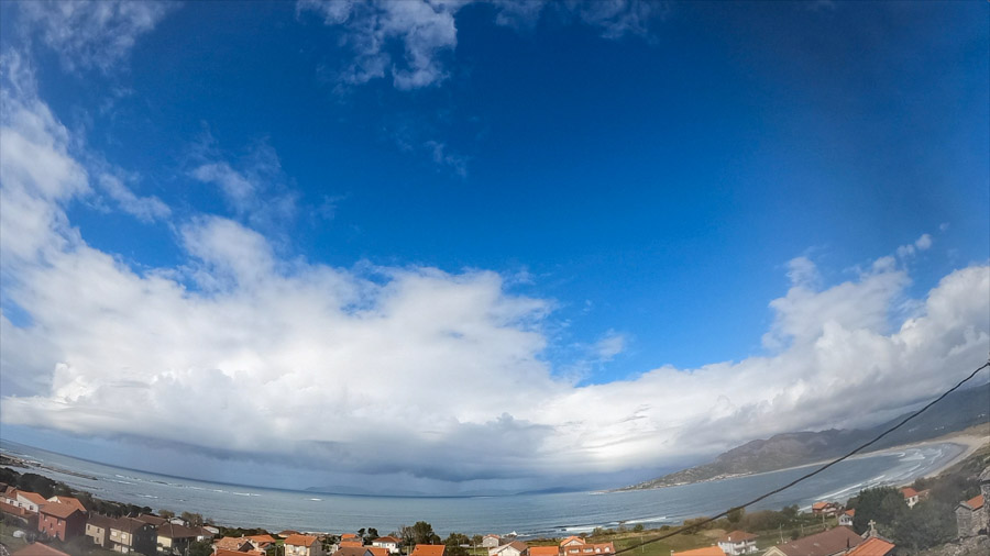 Panoramic daylight scene over Carnota Bay on the Costa da Morte with an overcast stratocumulus cloud layer broken by a blue sky hole above Sofán village, Monte Pindo, Caldebarcos and Cape Fisterra.
