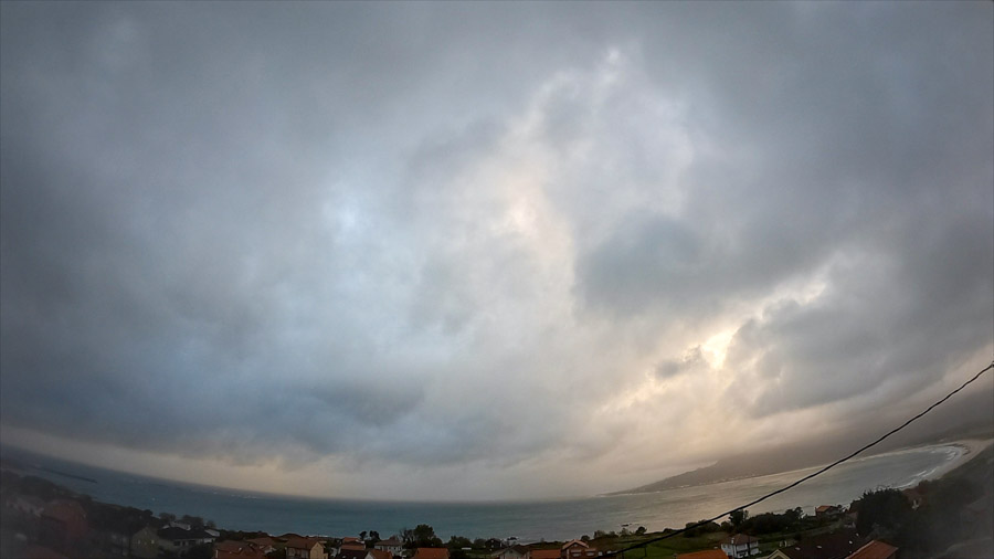 Late‑afternoon panoramic view over Carnota Bay on Galicia’s Costa da Morte with dark nimbostratus and stratocumulus clouds, rain haze and soft light over Monte Pindo, Caldebarcos and Cape Fisterra.