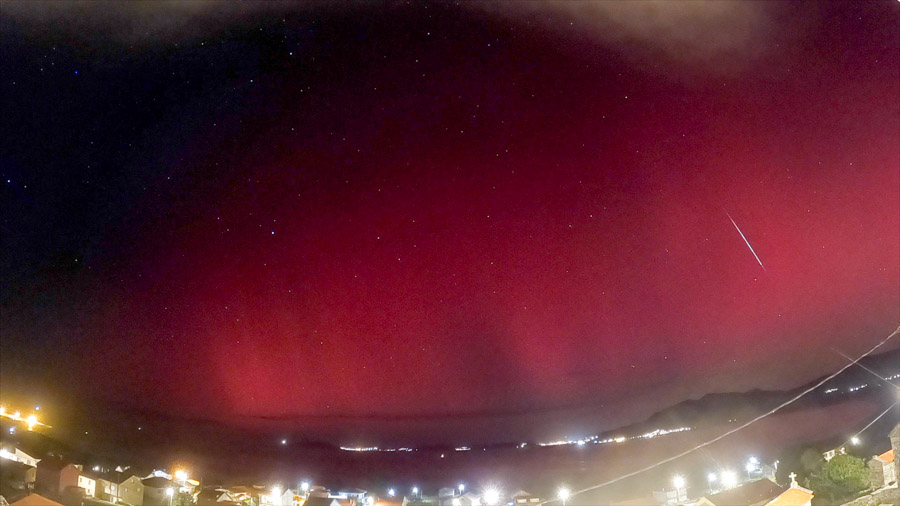 Panoramic night scene over Carnota Bay on Galicia’s Costa da Morte with intense red aurora borealis filling the sky and a bright meteor streaking down above the village lights of Sofán, Monte Pindo, Caldebarcos and Cape Fisterra.