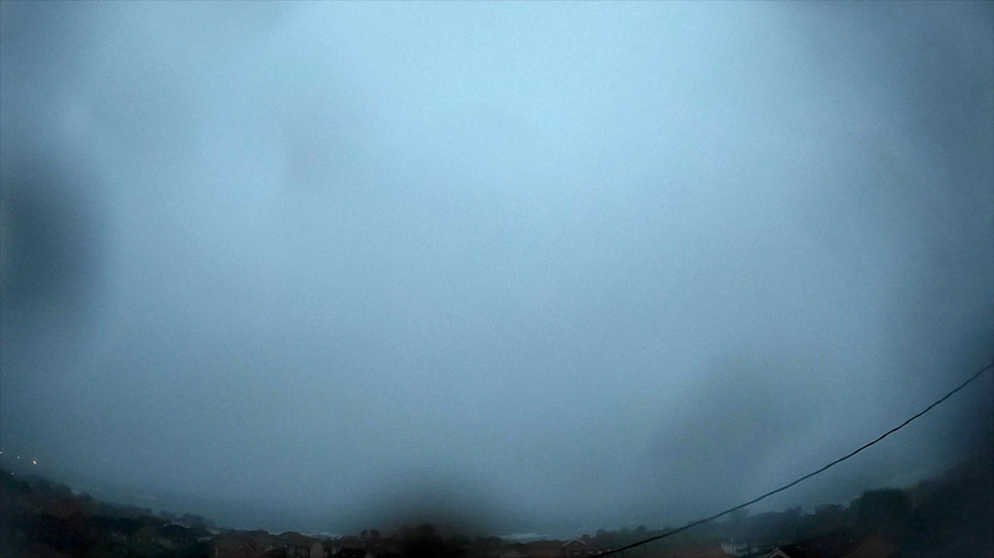 Very early‑morning view over Carnota Bay on the Costa da Morte with dense sea fog and low stratus cloud completely obscuring the sea, beach and Monte Pindo, seen faintly above Sofán village rooftops.